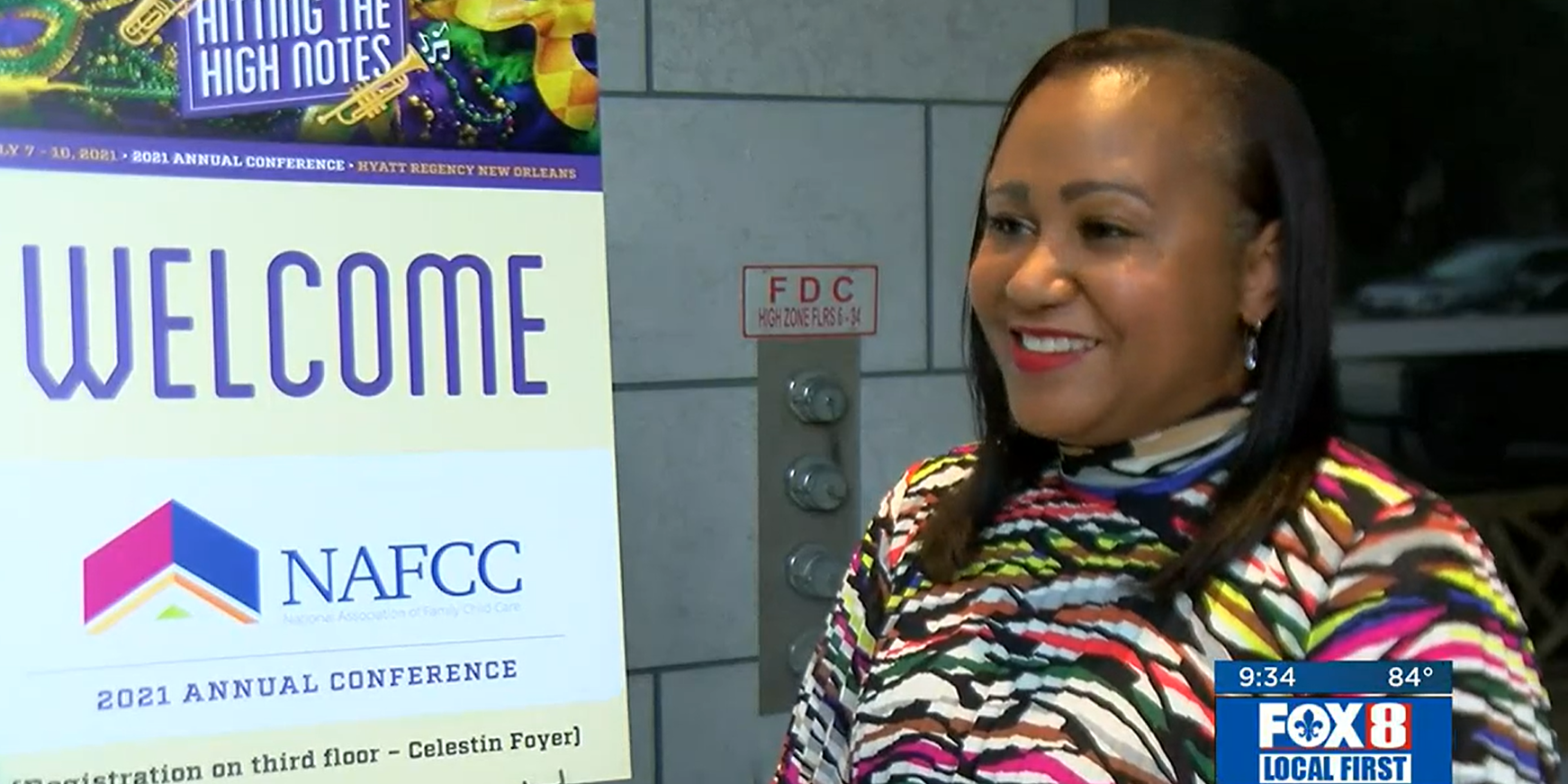 Executive Director Lanette Dumas smiling standing next to NAFCC "Hitting the High Notes" poster