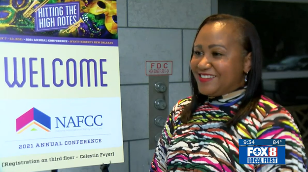 FOX8 Lanette Dumas Executive Director Lanette Dumas smiling standing next to NAFCC "Hitting the High Notes" poster